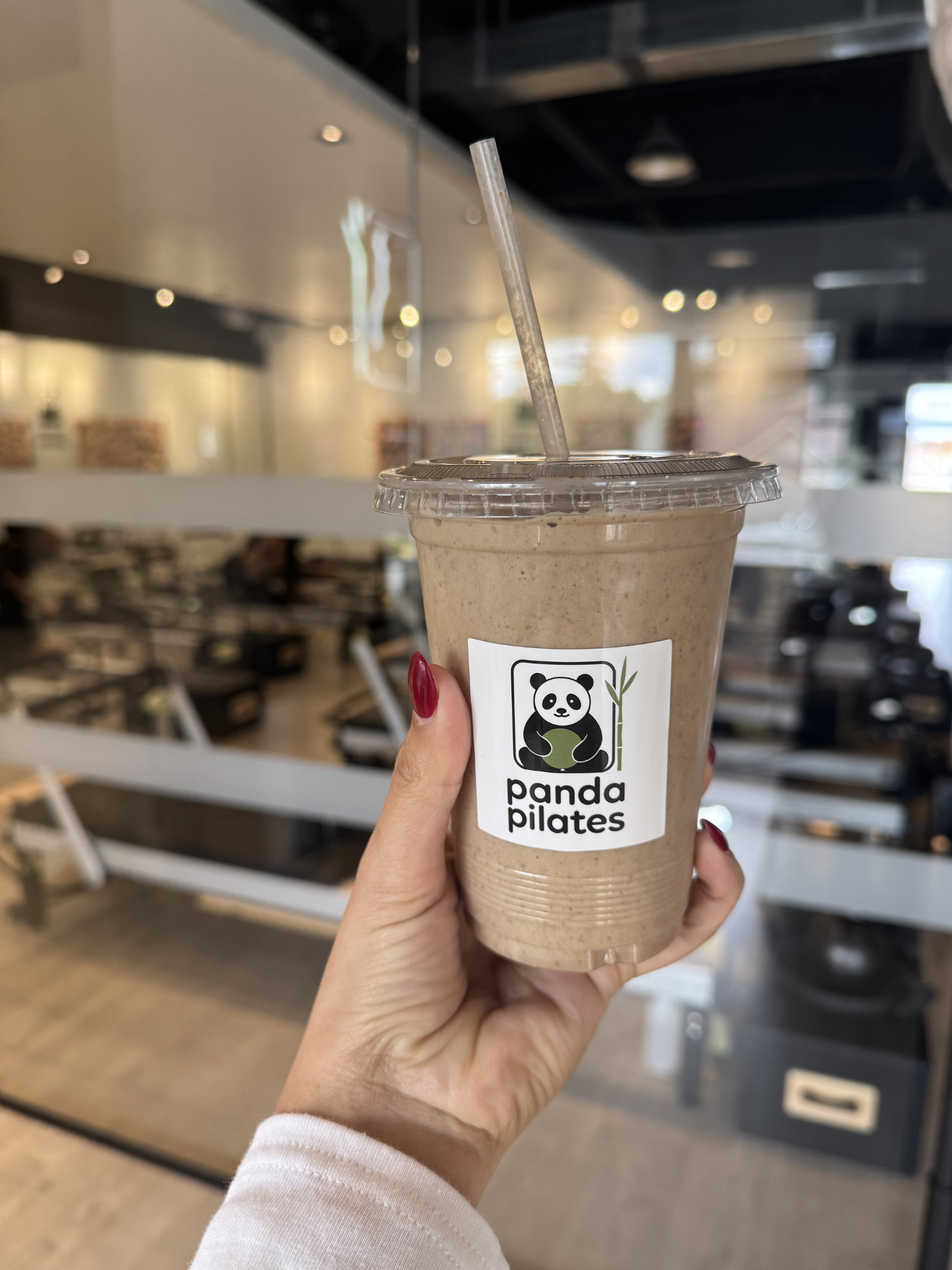 Hand holding a Panda Pilates protein shake in front of the reformer studio