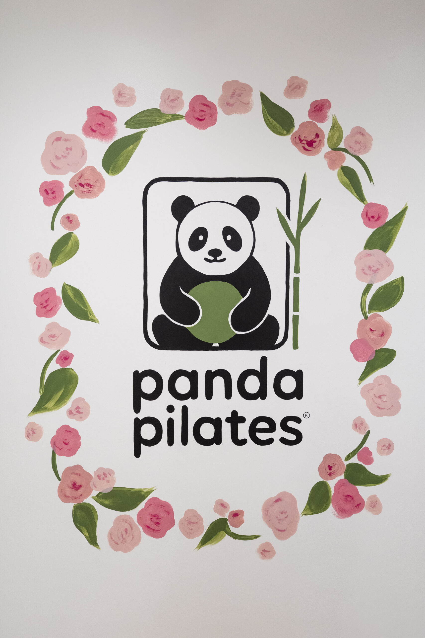 Hand-painted Panda Pilates logo mural with a panda holding a green Pilates ball, framed by pink roses